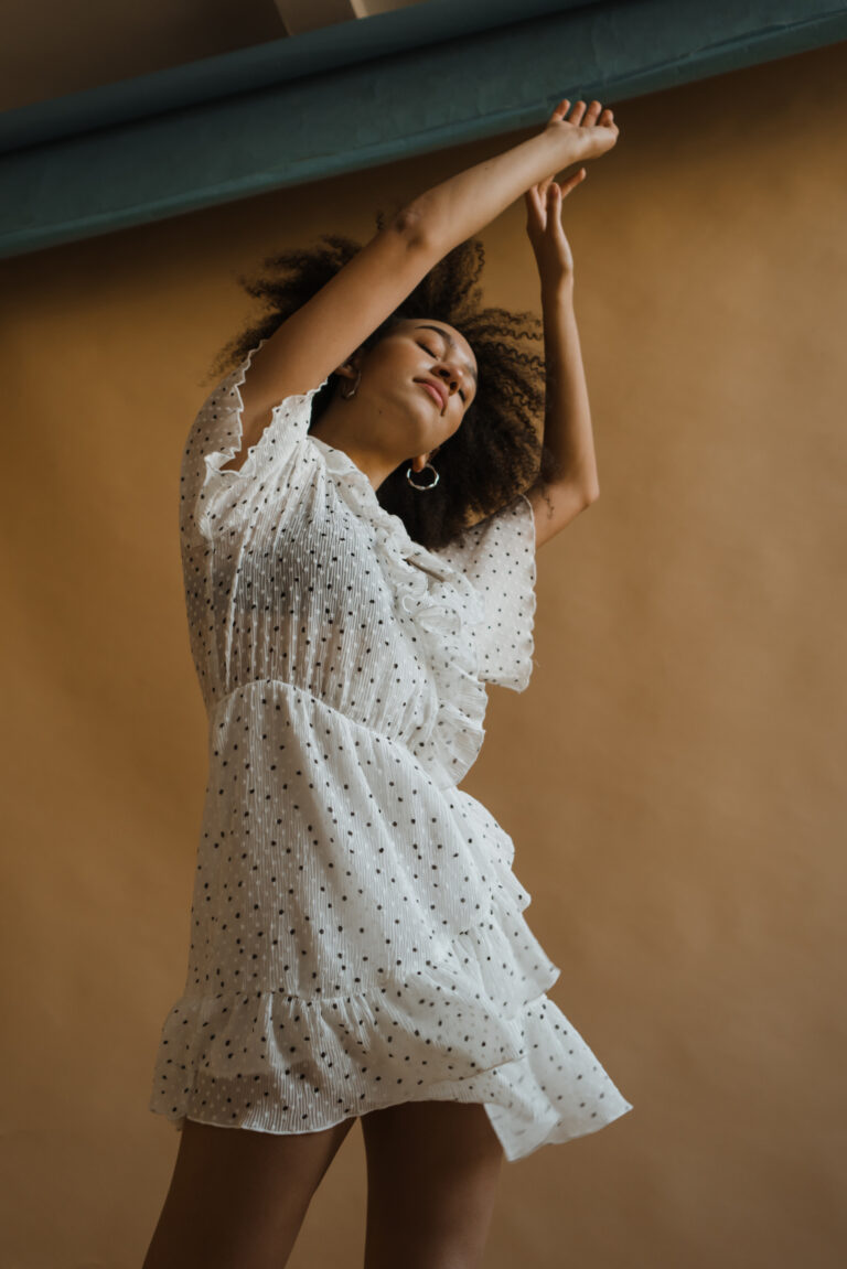 Woman in white lace dress dancing with her arms up and head tilted backwards.
