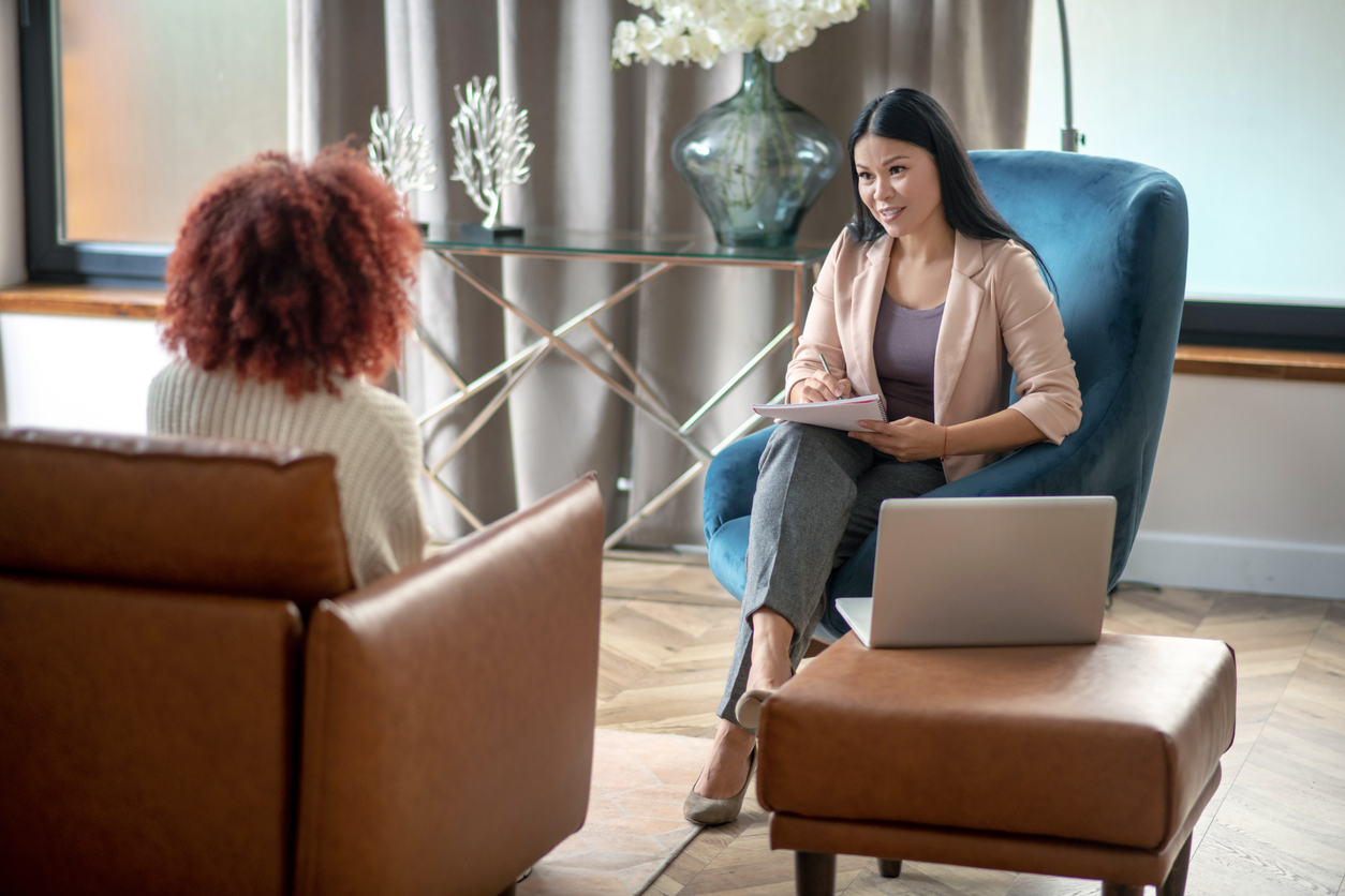 Dark-haired psychoanalyst. Dark-haired psychoanalyst sitting in armchair in front of patient and talking