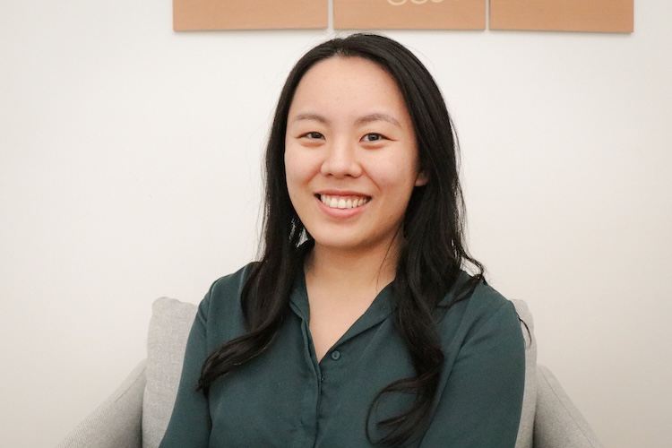 A smiling woman with light warm skin, brown eyes, and loosely waved black hair. She is wearing a dark green blouse.